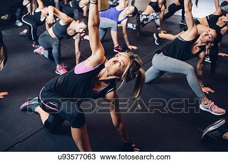 Stock Image - Group of women training in gym, bending forward with arm raised. Fotosearch