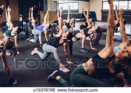 Stock Photo - Group of women training in gym, bending forward with arm raised. Fotosearch