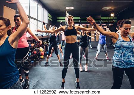 Stock Image - Group of women training in gym, jumping with arms outstretched. Fotosearch