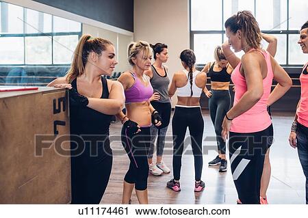 Stock Image - Group of women training in gym, taking a break chatting. Fotosearch