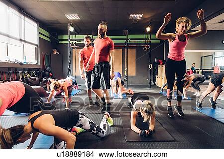Picture - Group of women training in gym with male trainers, doing squats. Fotosearch