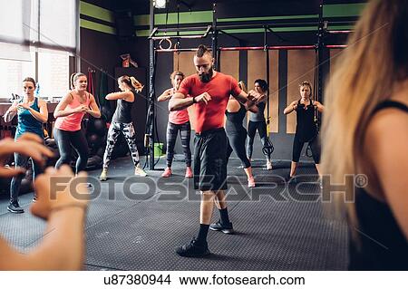 Picture - Group of women training in gym with male trainer, twisting. Fotosearch