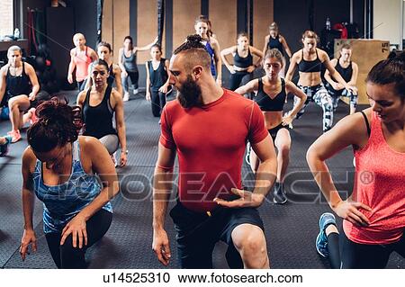 Stock Image - Group of women training in gym with male trainer, squatting. Fotosearch