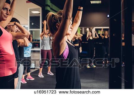 Stock Image - Group of women training in gym, with arms raised, side view. Fotosearch