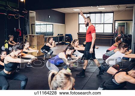 Stock Photo - Group of women training in gym with male trainer, squatting. Fotosearch