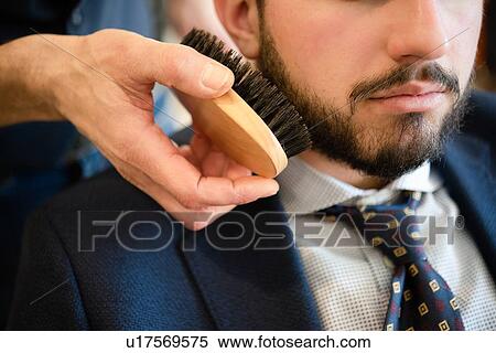Stock Photography - Hairdresser brushing customer's beard in barber shop. Fotosearch
