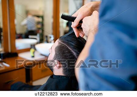 Stock Image - Hairdresser combing customer's hair in barber shop. Fotosearch