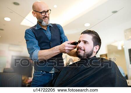 Stock Photography - Hairdresser shaving customer's hair in barber shop. Fotosearch