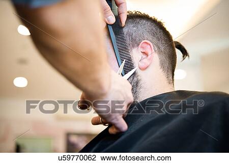 Stock Image - Hairdresser trimming customer's beard in barber shop. Fotosearch