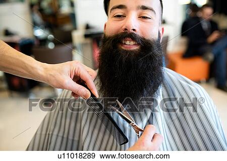 Stock Photo - Hairdresser trimming customer's beard in barber shop. Fotosearch