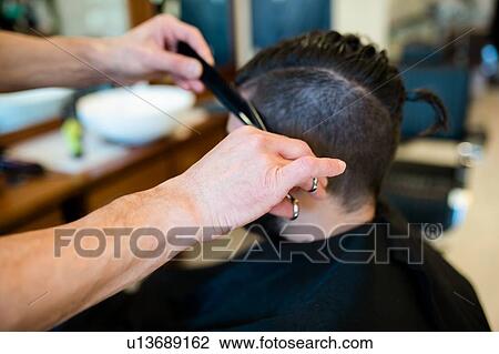 Stock Image - Hairdresser trimming customer's hair in barber shop. Fotosearch