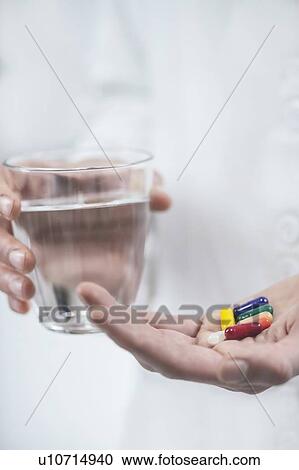 Stock Image - Hands with colourful pills and a glass of water. Fotosearch