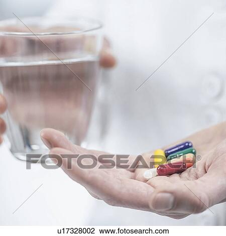 Stock Image - Hands with colourful pills and a glass of water. Fotosearch