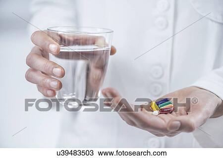 Stock Image - Hands with colourful pills and a glass of water. Fotosearch