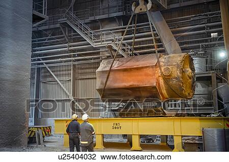 Stock Image - Hot 200 ton steel ingot being lifted onto transport to forge in steelworks. Fotosearch