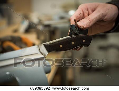 Stock Image - Knife factory worker applying wood stain to knife handle, close up of hands. Fotosearch