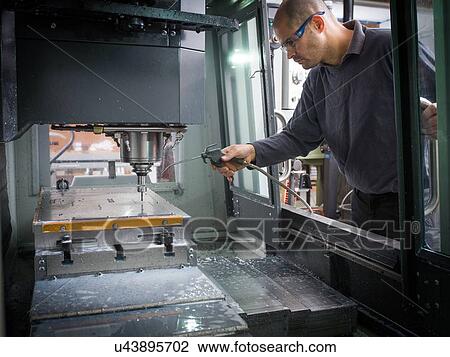 Stock Image - Knife factory worker operating cutting machinery. Fotosearch