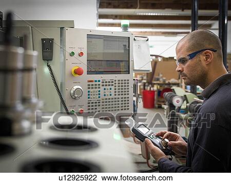 Stock Image - Knife factory worker operating machinery controls. Fotosearch
