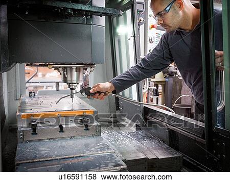 Stock Photo - Knife factory worker spraying liquid onto machinery in workshop. Fotosearch