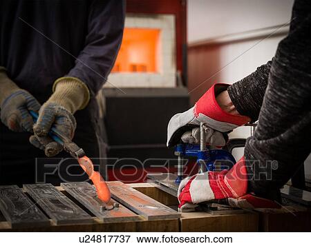 Stock Photo - Knife factory workers using tongs to remove red hot metal from mould in workshop, close up of hands. Fotosearch