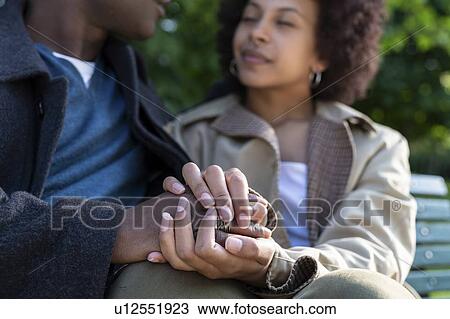 Stock Image - Loving couple holding hands on park bench, Milan, Italy. Fotosearch