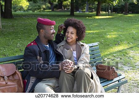Stock Photo - Loving couple holding hands on park bench, Milan, Italy. Fotosearch