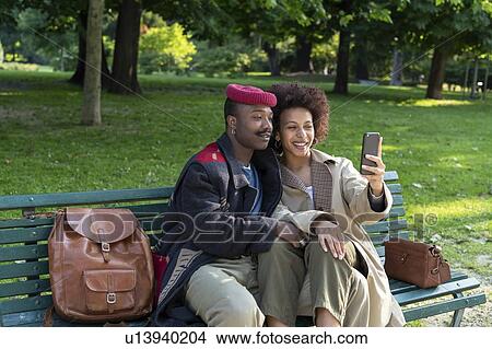 Picture - Loving couple taking selfie on park bench, Milan, Italy. Fotosearch