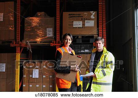 Stock Photography - Male and female factory workers with clipboard in warehouse, portrait. Fotosearch