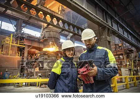 Male and female steelworkers using digital tablet during steel pour in steelworks View Large Photo Image Stock Photograph - Male and female steelworkers using digital tablet during steel pour in steelworks. Fotosearch