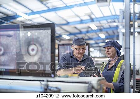 Stock Image - Male and female workers checking print output in print factory. Fotosearch