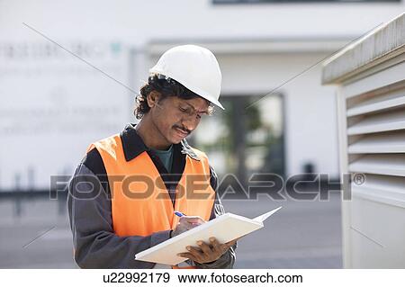 Male engineer outside industrial building writing in notebook View Large Photo Image Stock Photo - Male engineer outside industrial building writing in notebook. Fotosearch
