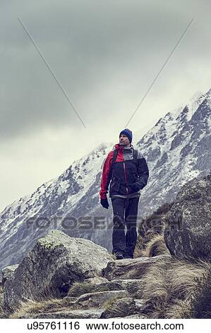 Stock Photograph - Male hiker hiking in rugged landscape with snow capped mountains, Llanberis, Gwynedd, Wales. Fotosearch