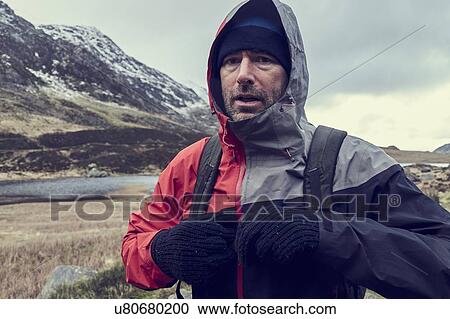 Stock Image - Male hiker with hood up in snow capped mountain landscape, portrait, Llanberis, Gwynedd, Wales. Fotosearch