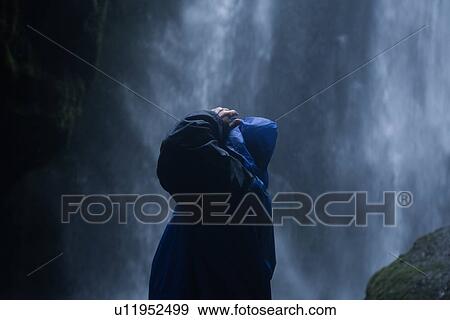 Stock Photo - Male tourist wearing hooded anorak looking up at waterfall, Selfoss, Arnessysla, Iceland. Fotosearch