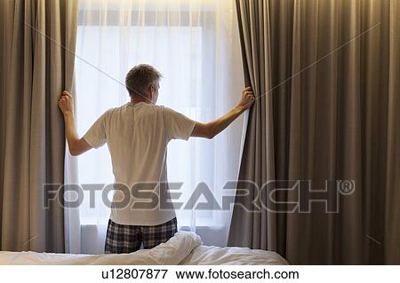 Man opening curtains in hotel room View Large Photo Image Stock Photo - Man opening curtains in hotel room. Fotosearch