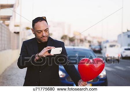 Man photographing red heart shaped balloon View Large Photo Image Stock Image - Man photographing red heart shaped balloon. Fotosearch
