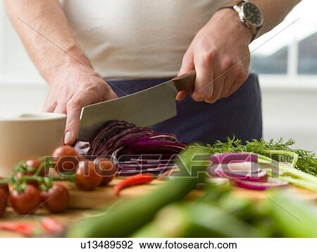 Stock Image - Man slicing red cabbage at kitchen counter, mid section. Fotosearch