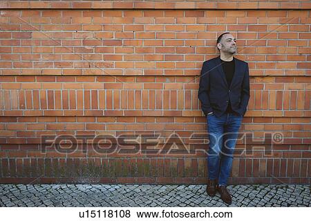 Stock Photo - Man wearing blazer and jeans by brick wall. Fotosearch
