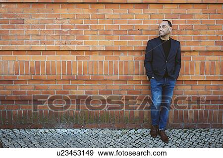 Stock Photo - Man wearing blazer and jeans by brick wall. Fotosearch