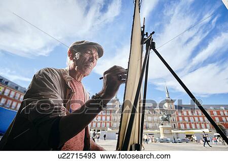 Stock Image - Mature male street artist drawing on canvas in town square, Madrid, Spain. Fotosearch