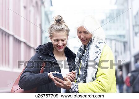 Stock Photo - Mature woman and daughter looking at smartphone on city street. Fotosearch