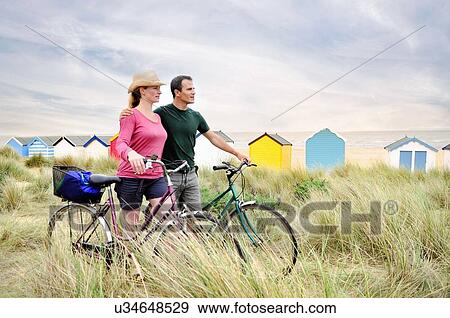 Stock Photo - Mid adult couple with bicycles at coast, Southwold, Suffolk, UK. Fotosearch