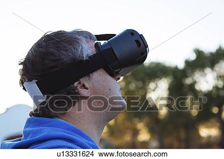 Picture - Mid adult man wearing virtual reality simulator outdoors. Fotosearch