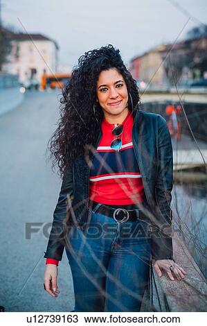 Mid adult woman with long curly hair by city canal, portrait View Large Photo Image Stock Image - Mid adult woman with long curly hair by city canal, portrait. Fotosearch