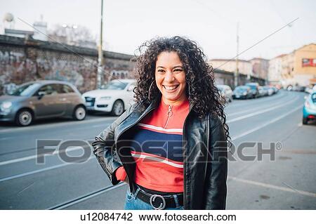 Stock Image - Mid adult woman with long curly hair on city sidewalk. Fotosearch