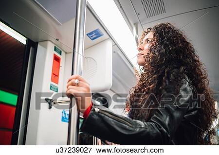 Stock Photo - Mid adult woman with long curly hair on city subway train. Fotosearch
