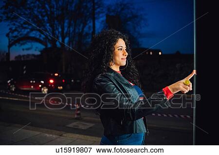 Mid adult woman with long curly hair using illuminated touchscreen at city bus stop at night View Large Photo Image Stock Photo - Mid adult woman with long curly hair using illuminated touchscreen at city bus stop at night. Fotosearch