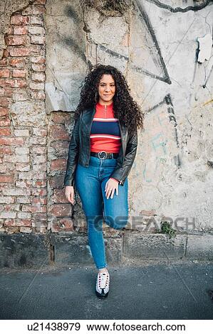 Mid adult woman with long curly hair leaning against wall on city sidewalk, portrait View Large Photo Image Stock Photo - Mid adult woman with long curly hair leaning against wall on city sidewalk, portrait. Fotosearch