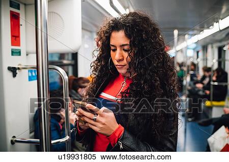 Mid adult woman with long curly hair looking at smartphone on city subway train View Large Photo Image Stock Photography - Mid adult woman with long curly hair looking at smartphone on city subway train. Fotosearch