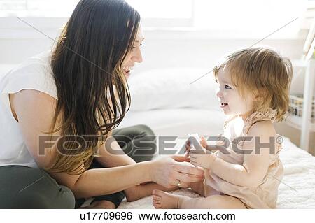 Stock Photograph - Mother and daughter on bed with hairbrush. Fotosearch
